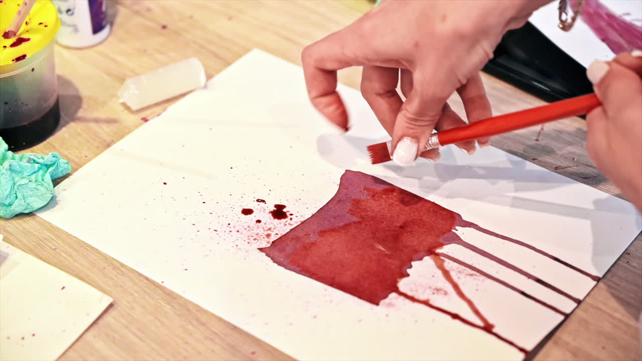 A woman in a studio painting on paper with red wine and brush, close view, slow motion