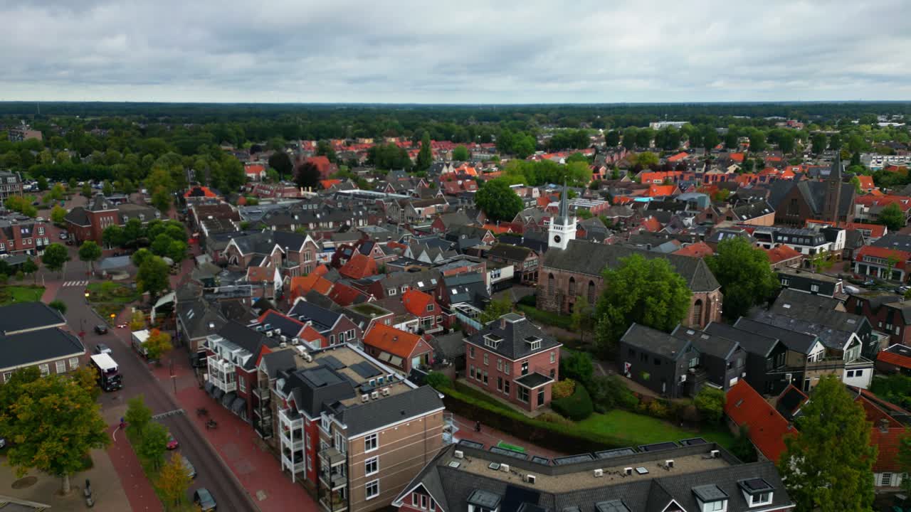 Wide aerial panorama of Ommen showing clustered red rooftops, church towers, and tree-lined horizon beneath a cloudy sky. Location: Ommen, Overijssel, Netherlands (Ommen, Overijssel, Nederland)