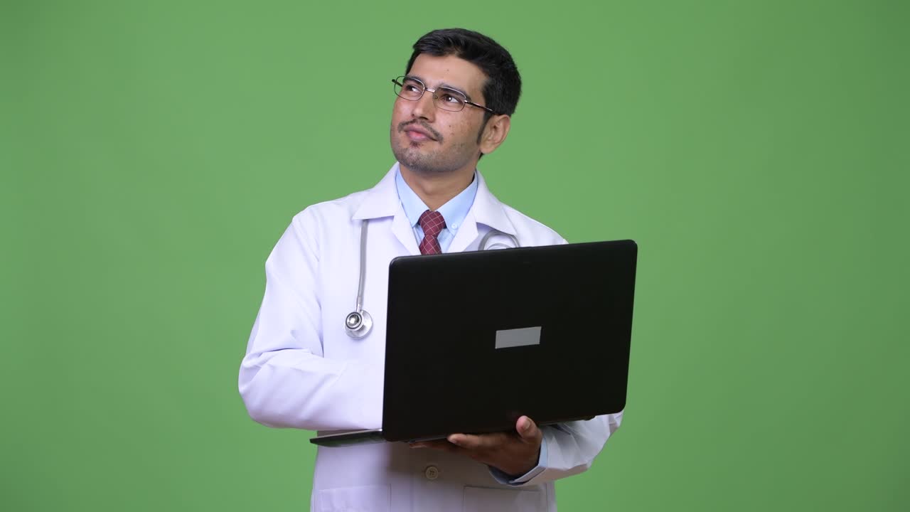 Young handsome Persian man doctor using laptop