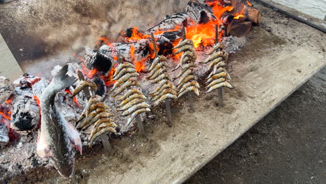 Traditional-Spanish-sardines-Espetos-fish-grilled-at-the-beach-over-fire-on-metal-skewers-in-Marbella-Malaga-Spain,-delicious-seafood,-4K-static-shot