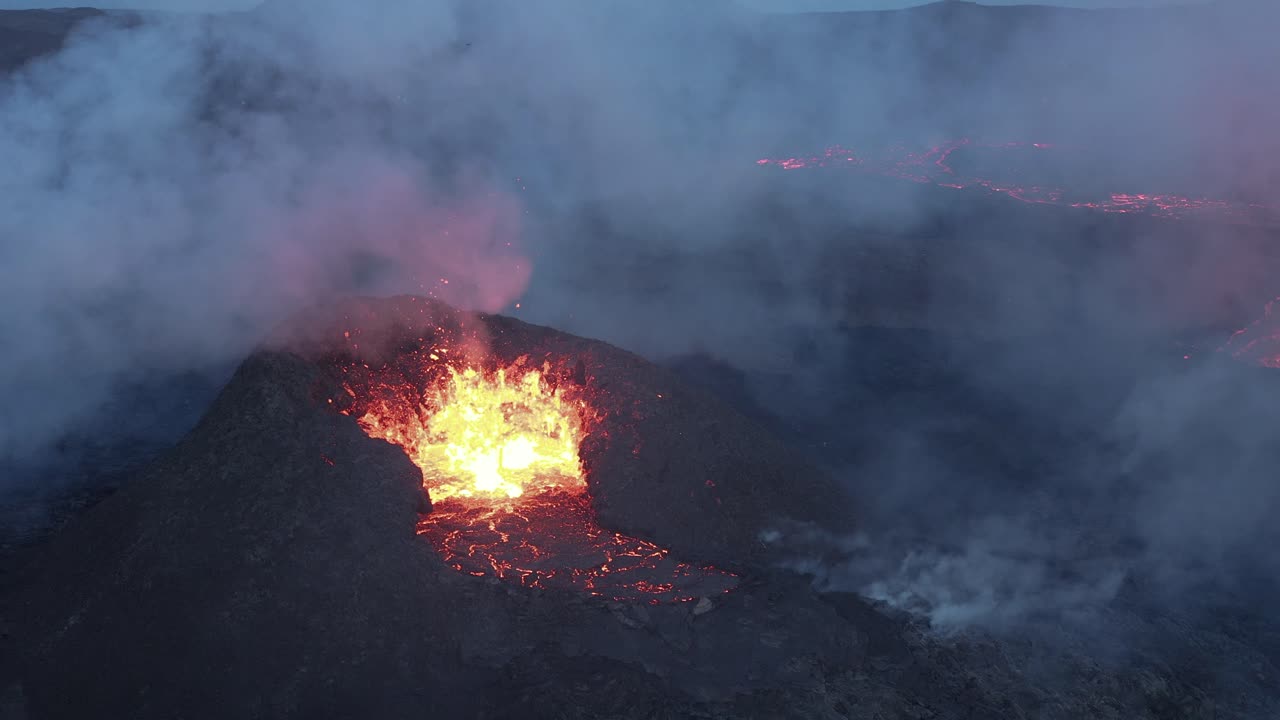 Clouds of smoke surrounding black crater mound with erupting lava in Iceland