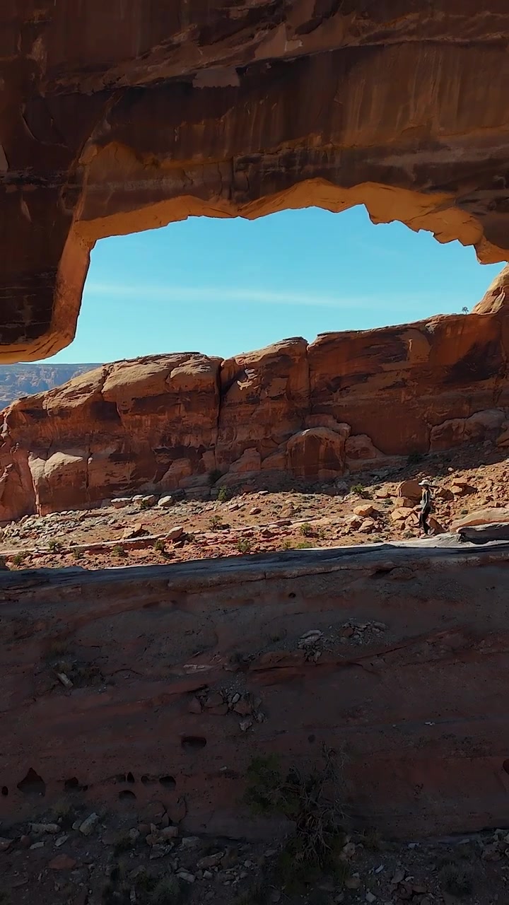 Jeep Arch, Utah USA. Ripresa verticale con drone che rivela una donna che cammina sotto un punto di riferimento panoramico nel deserto