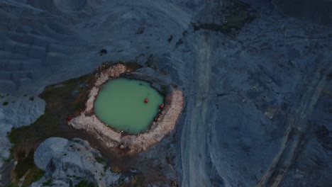 beautiful drone view of captured secluded quarry pool amidst rugged terrain. the aerial view showcases vivid turquoise water surrounded by rocky landscape at dusk, creating a serene dramatic scene