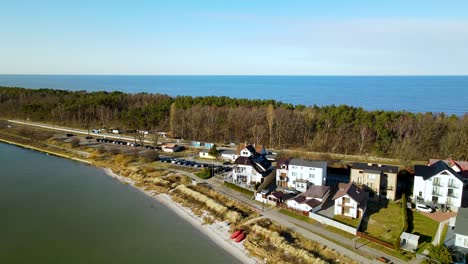 aerial drone shot of beautiful narrow island of hel with road,houses and forest trees during sunny day - blue baltic sea in background