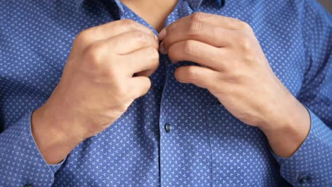 man buttoning a blue dress shirt