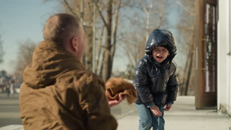 cerca de un niño arrojando el gorro de su padre de vuelta a él felizmente como el padre, inclinándose, extiende su mano izquierda y lo atrapa