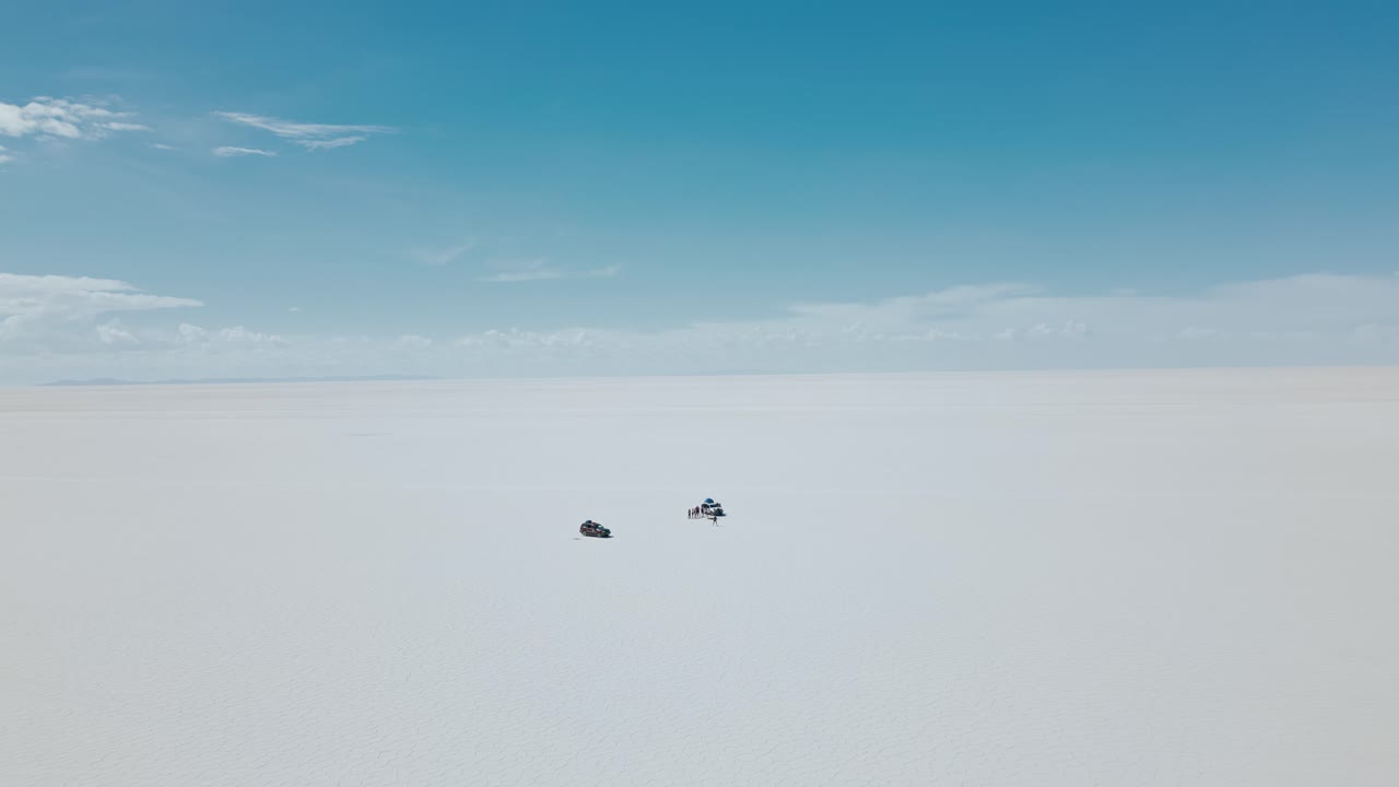 Marvel at the vast expanse of Bolivia's Salar de Uyuni with stunning drone footage capturing small jeeps traversing the endless salt flats from above