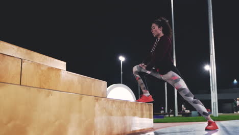 chica rizada deportiva haciendo estocadas en las escaleras en el parque por la noche