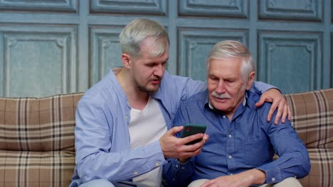 Happy-family-senior-father-and-son-watching-on-mobile-phone-to-internet-online-with-fun-together