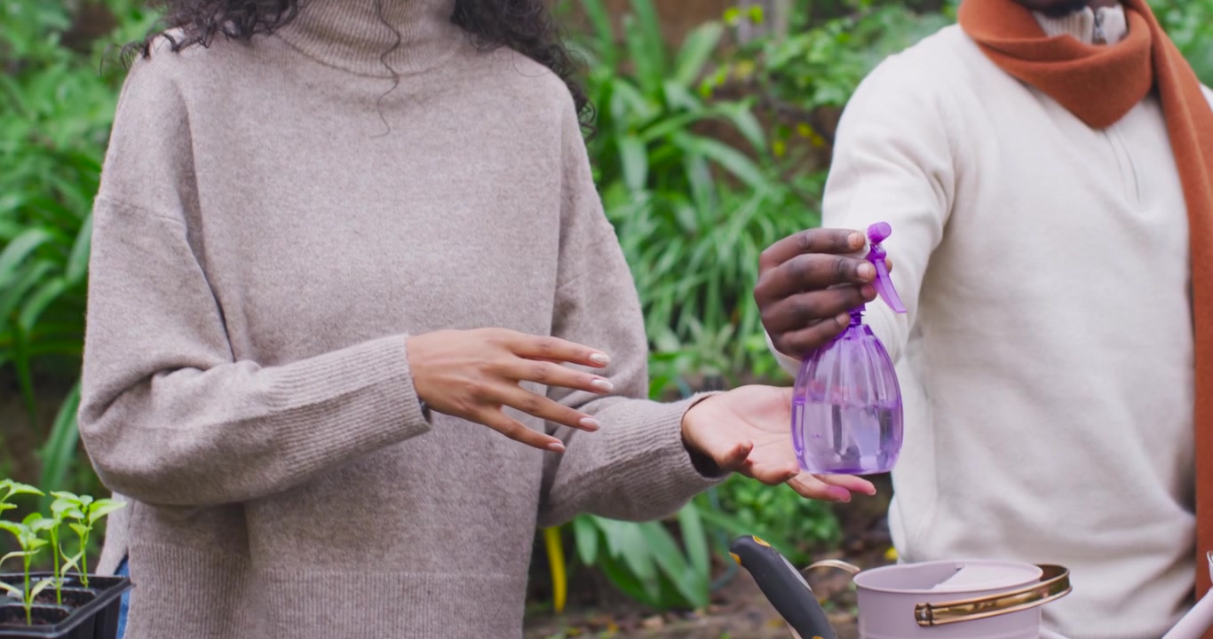 Amici di diverse etnie a un tavolo da giardino, uomo che offre uno spruzzino viola, donna che mostra come nebulizzare le piantine