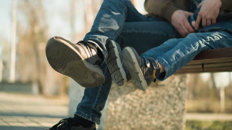 close-up shot of an adult and a child sitting closely together, with the adult's legs crossed and the child playfully hanging his right leg over the adult's crossed leg while dangling the left leg