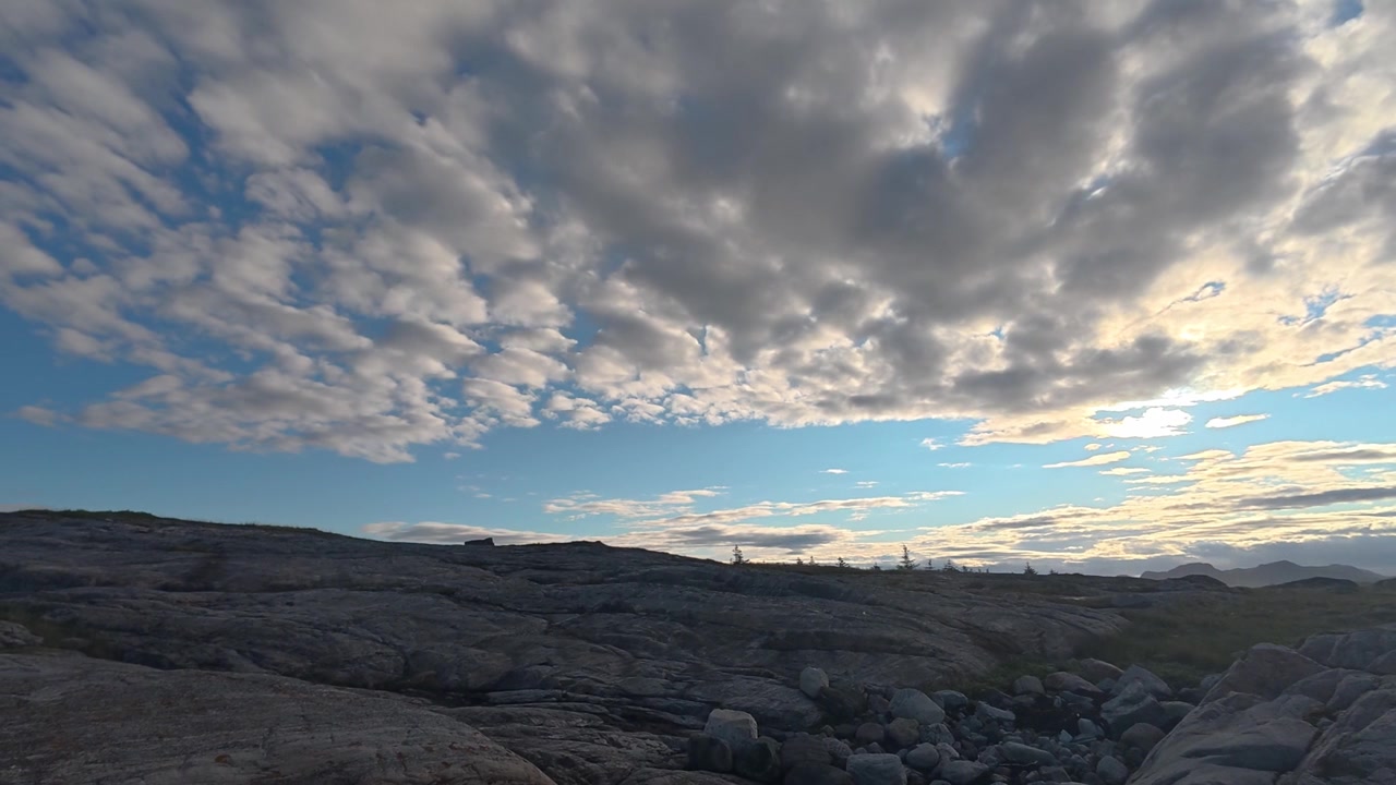 Leggera copertura di nubi altocumulo si estende su un paesaggio costiero roccioso