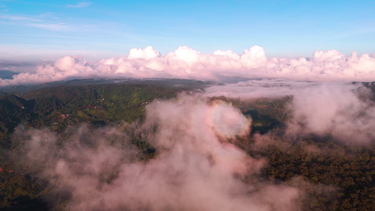 Spectacular aerial view of a dense,hilly, tropical forest landscape at sunrise or sunset. Beautiful pink-hued clouds and fog roll over the terrain, casting long shadows and creating a dramatic