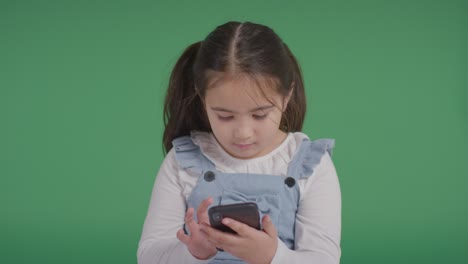 Studio-Portrait-Of-Young-Girl-On-ASD-Spectrum-Playing-With-Mobile-Phone-On-Green-Background