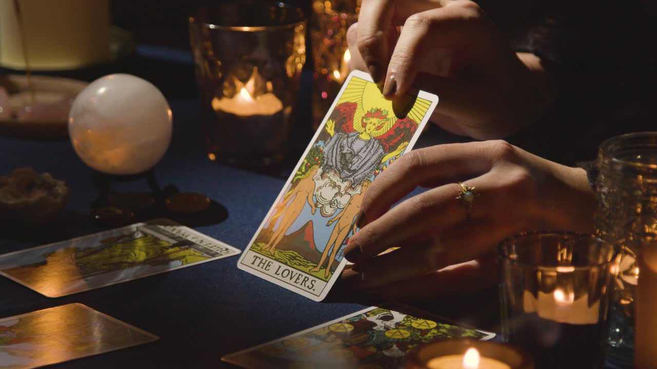 un primer plano de una mujer dando una lectura de tarot en una mesa a la luz de las velas sosteniendo la carta de los amantes 1