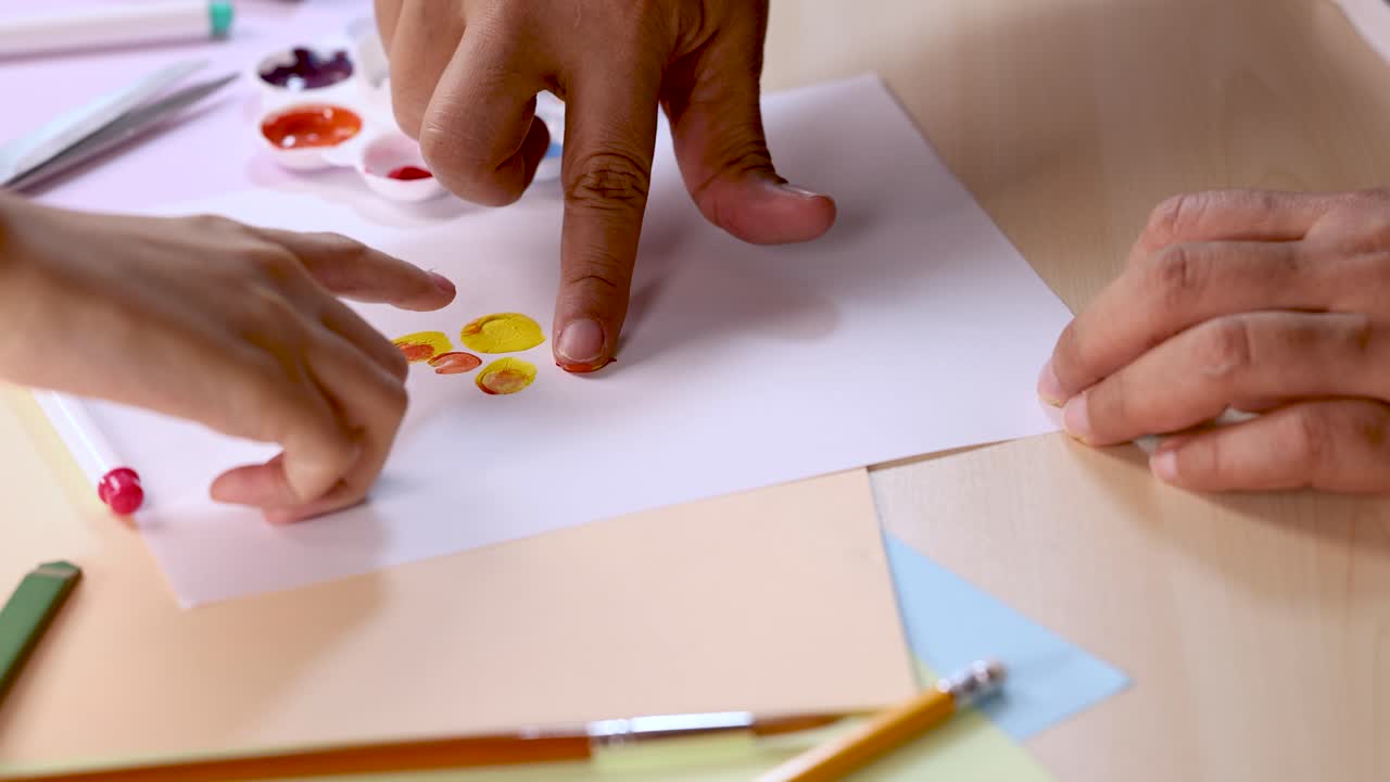 Hands dab paint and press fingerprints onto paper, bright lighting, overhead camera, creative art activity