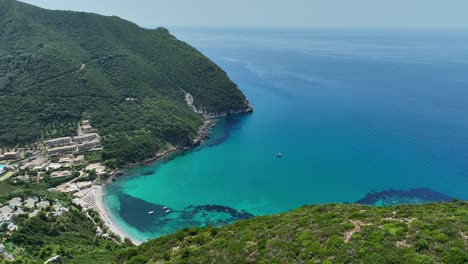 Coastline-of-Corfu-Island-with-turquoise-waters,-boats,-and-green-hills,-aerial-view