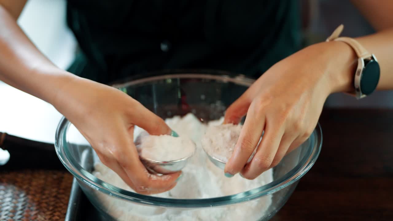 A woman's hands carefully mix white powder ingredients in a glass bowl, a close-up of the creative process of making natural, homemade soap ball during an artisanal craft workshop or class