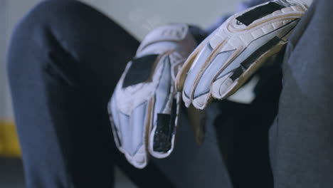 close-up of hands wearing white sports gloves resting on knees of person sitting in casual sportswear, yellow marking on metallic fence in background