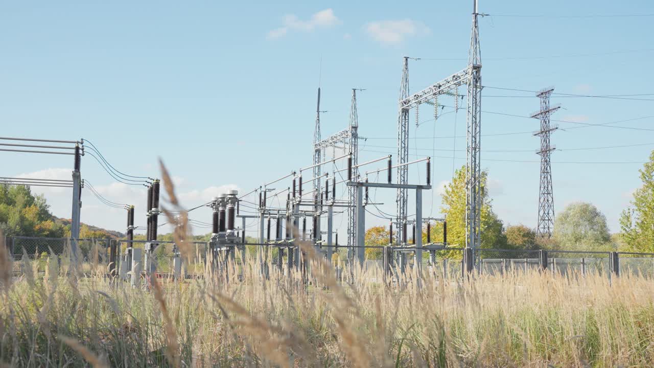 High-voltage electrical substation in a rural field surrounded by dry grass under a clear blue sky, showcasing energy infrastructure and power distribution network