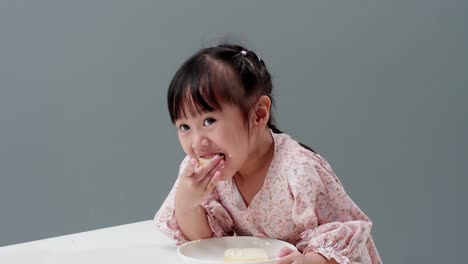 Asiatic-child-eating-piece-of-sweet-in-the-studio-with-a-gray-background