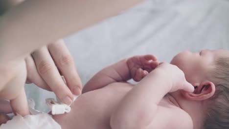 el bebé se acuesta en la cama y la madre desinfecta el cordón umbilical