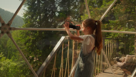 niño graba video de la naturaleza en glamping. niña con cámara filma escena del bosque en un hotel ecológico. niño juega a videógrafo en vacaciones de verano