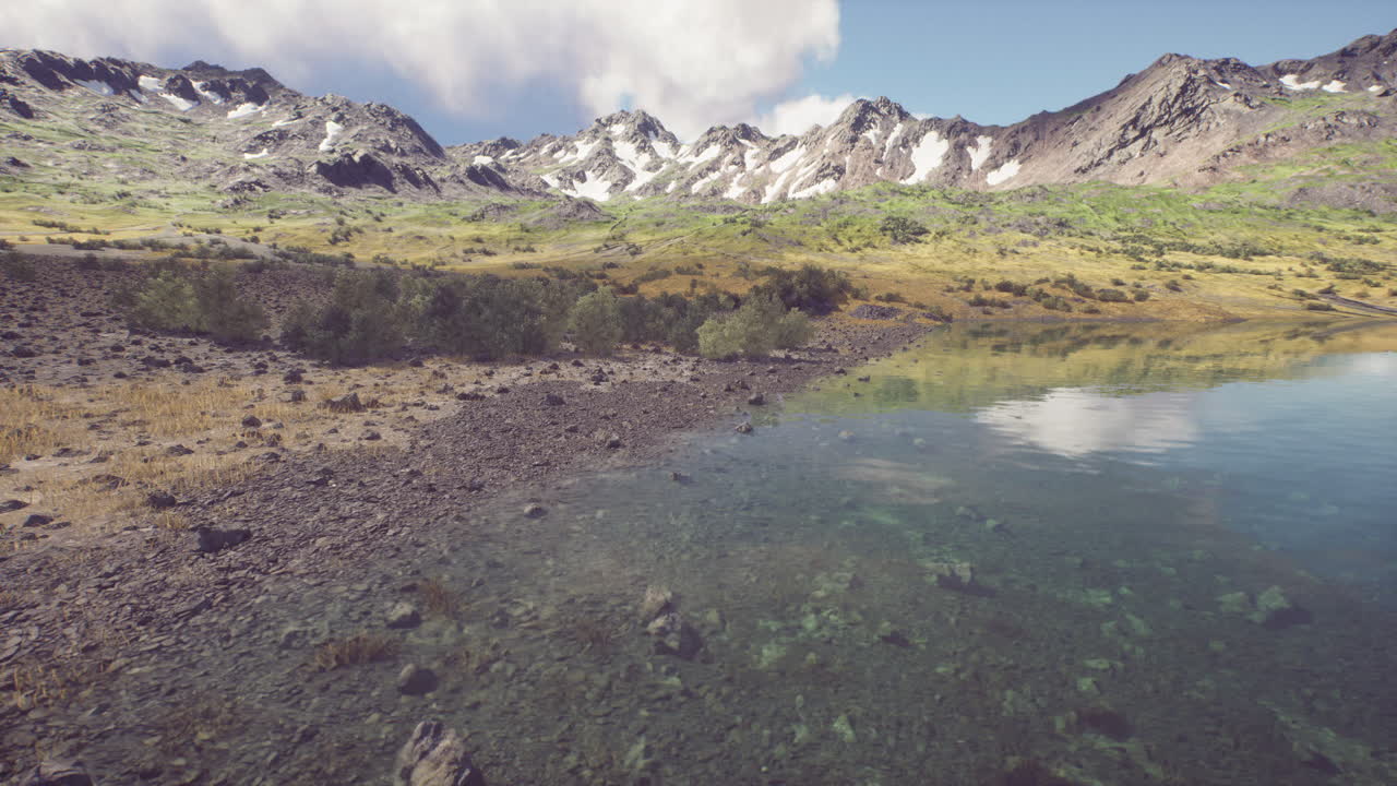 Lush mountain landscape with clear lake reflecting clouds in summer sunlight