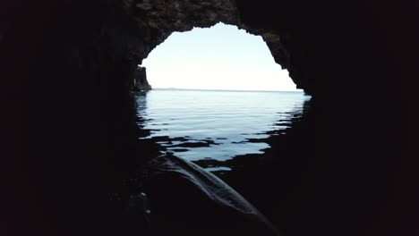 kayaker looking out to the horizon from the inside of a sea cave vis island, adriatic sea, croatia