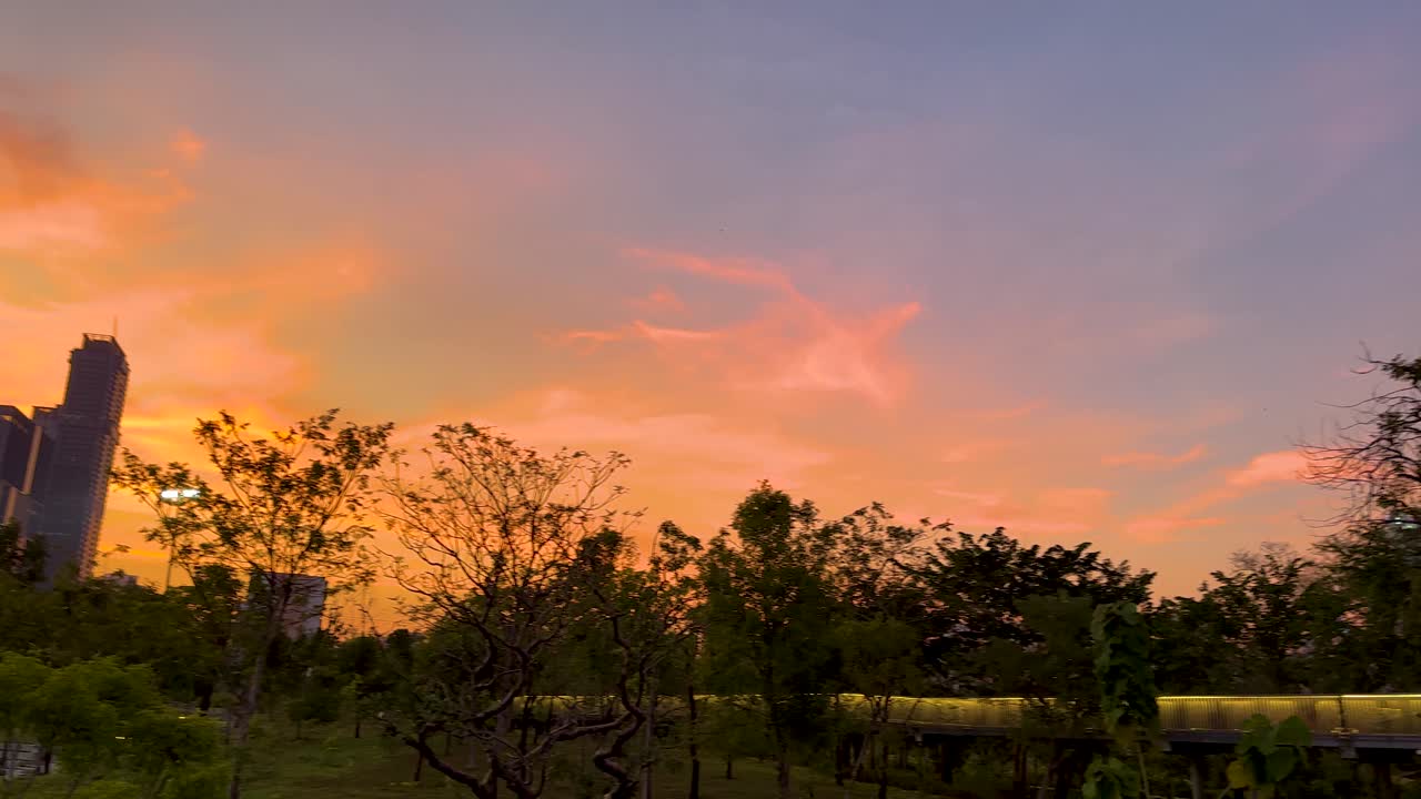 Vibrant sunset hues illuminate Bangkok's skyline and lush greenery, creating a serene and picturesque evening scene