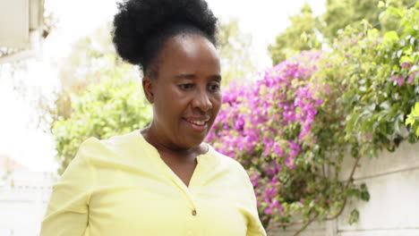 Feliz-Mujer-Mayor-Afroamericana-Caminando-Y-Sonriendo-En-Un-Jardín-Soleado,-Cámara-Lenta