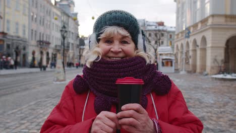 Portrait-of-senior-woman-tourist-smiling,-looking-at-camera-in-winter-city-center-of-Lviv,-Ukraine