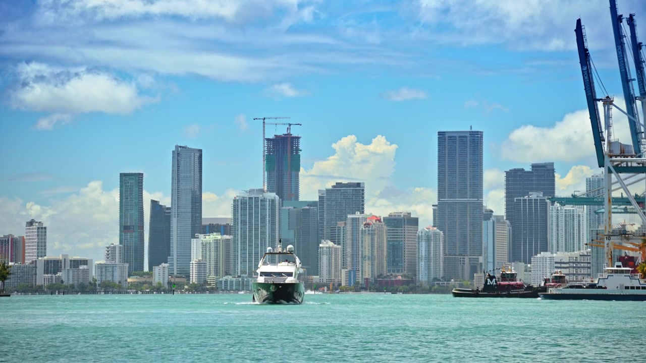 Miami, USA, 16 aprile 2026: Yacht a motore che naviga verso lo skyline di Miami in una giornata di sole, Florida. Imbarcazione bianca su acqua turchese con grattacieli e cielo azzurro con nuvole.