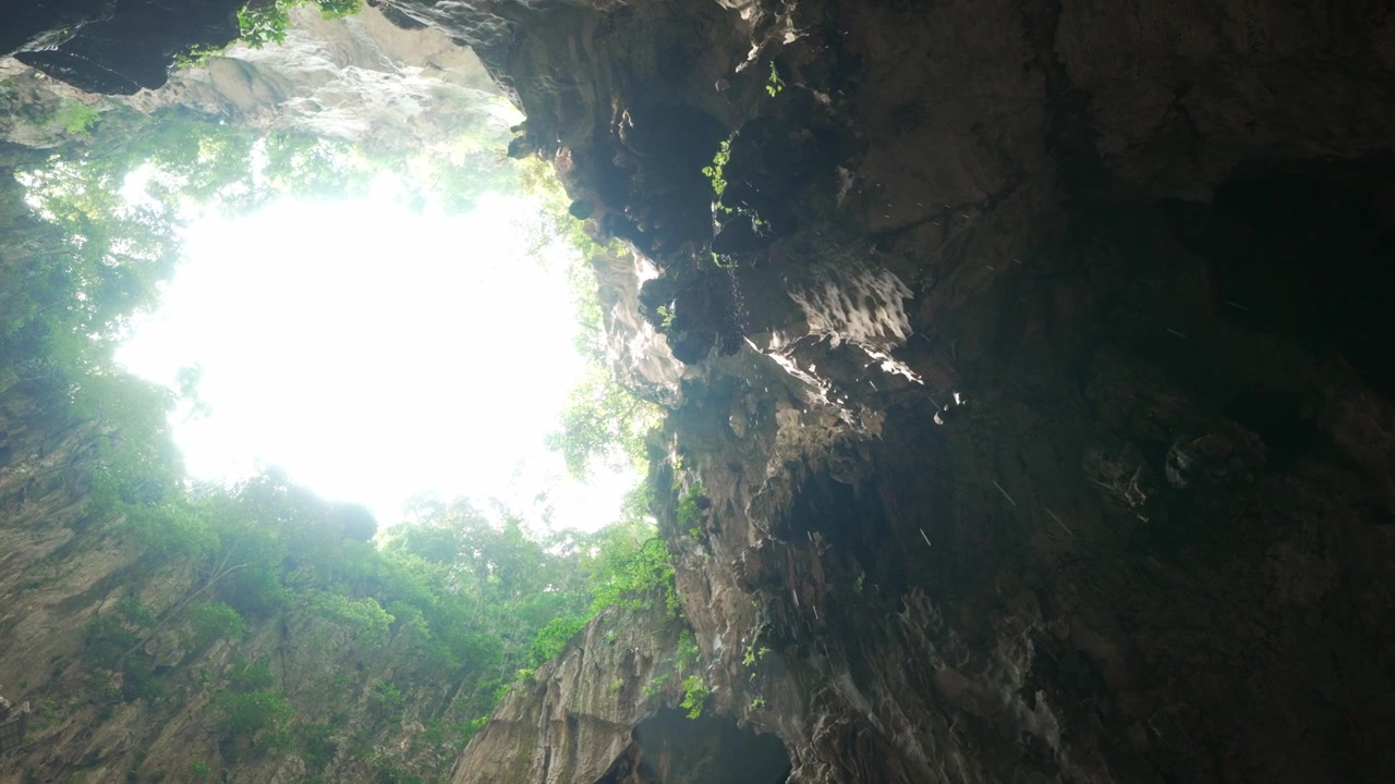 Cinematic perspective looking up through a cave opening with dripping water and sunlight filtering through.