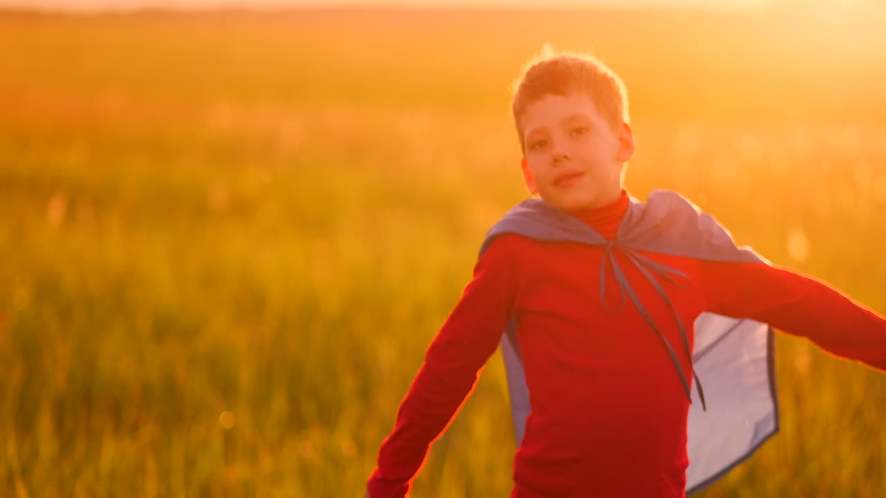 un niño vestido como un superhéroe de pie con una máscara y una capa roja corre riendo de la puesta de sol en el campo de verano. noche de verano el niño sueña y hazañas heroicas y cómics