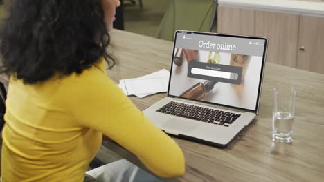 Biracial-woman-at-table-using-laptop,-online-shopping-for-beauty-products,-slow-motion