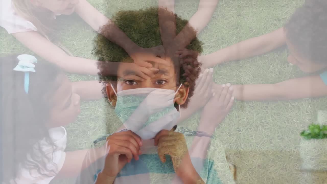 공원에서 손 스택을 하는 아이들의 그룹에 대항하여 얼굴 마스크를 쓰고 있는 아프리카계 미국인 소년