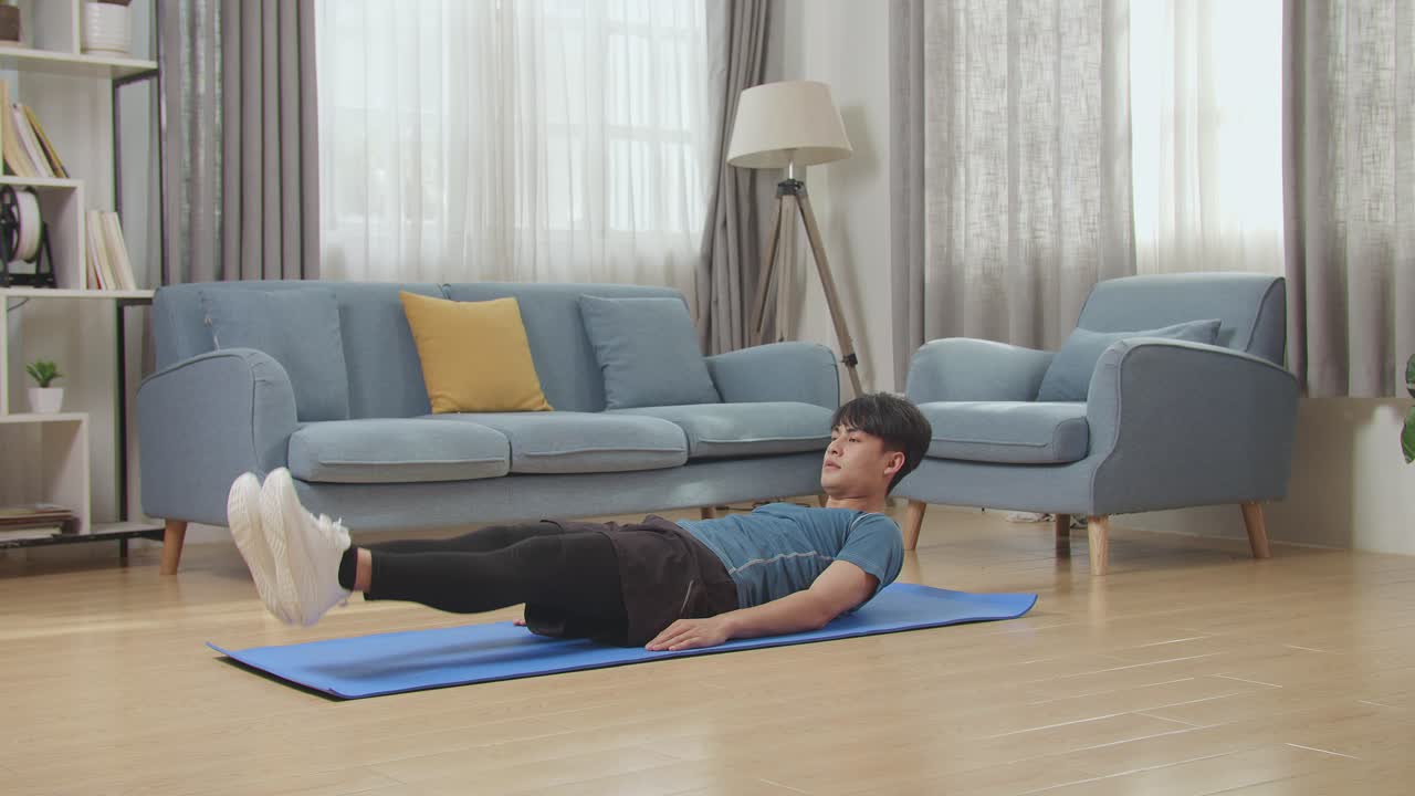 스포츠 옷을 입은 아시아인 남자가 집에서 복부 운동을 하고 있습니다.