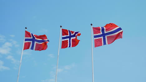 tres banderas noruegas revoloteando en el viento en cámara lenta con el cielo azul en el fondo