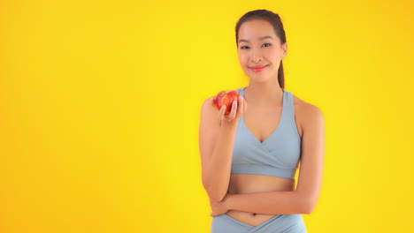 asian female in gym sportswear with fresh red apple, slow motion, healthy food and lifestyle concept, static shot isolated on yellow background