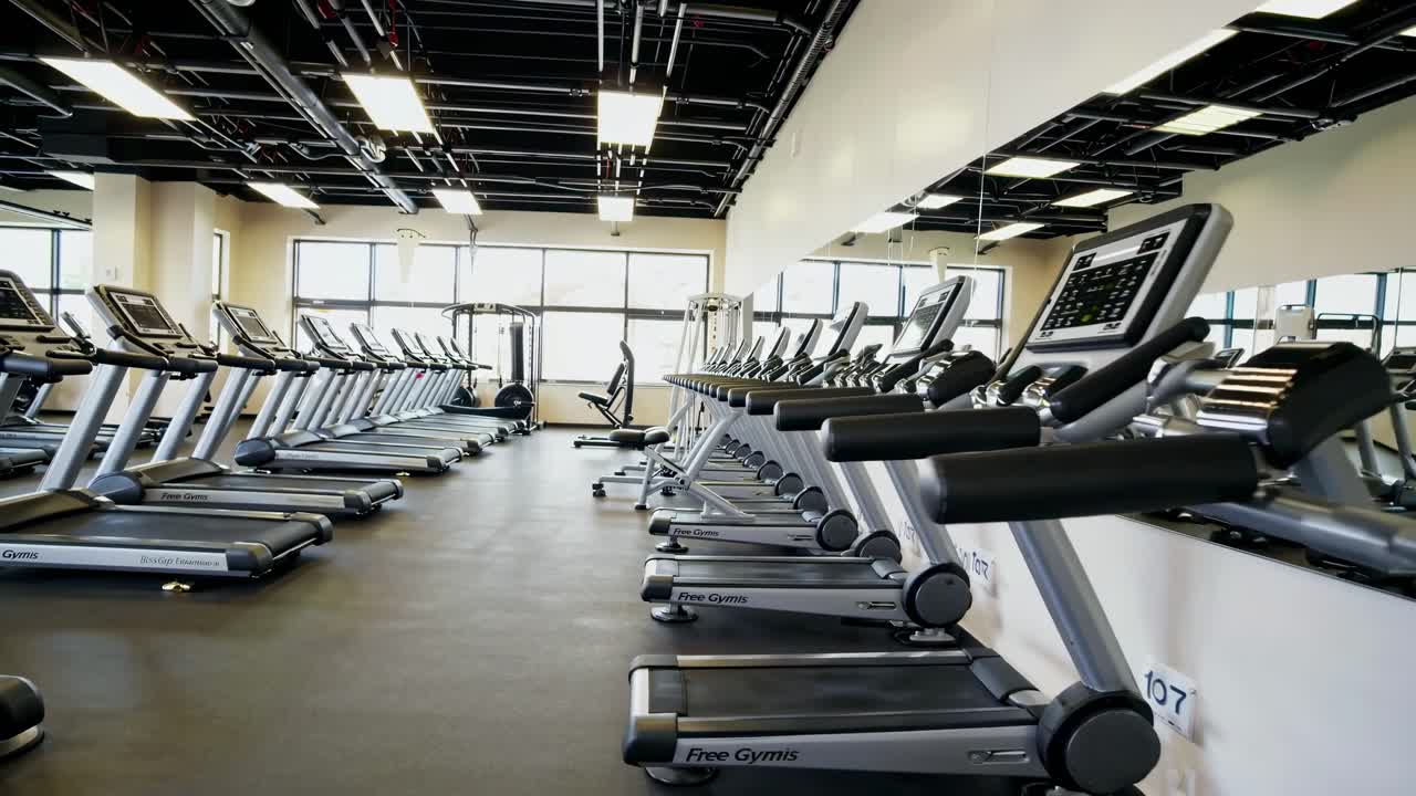 Wide-angle shot of a modern gym with rows of treadmills, reflecting in mirrors