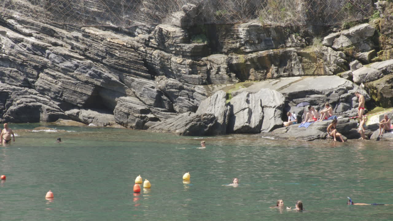 People On The Rugged Shore Of Vernazza Town In Cinque Terre, Northwest Italy, Ligurian Coast. Sideways Shot