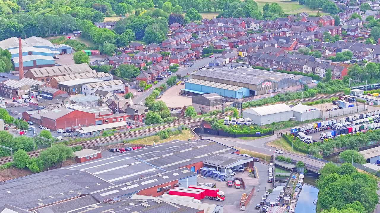 Aerial view over Stoke showing train passing by railway tracks, industrial warehouses in foreground and suburban housing in background, mix of industry and community on bright clear day