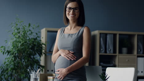 pregnant businesswoman caressing her belly and smiling to the camera