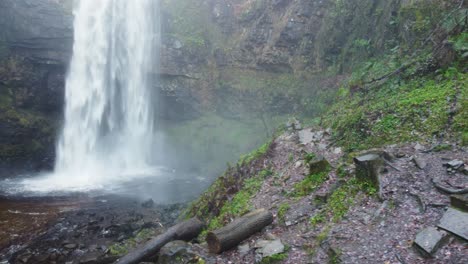 Sideways-Aerial-Drone-of-Dramatic-Waterfall-with-Warning-Sign-and-Chopped-Tree-Logs-4K