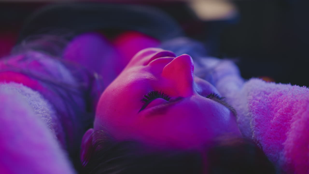close up of woman peacefully sleeping in studio while vibrant neon light highlights her calm face and soft textures of her outfit in relaxing creative environment with dreamy ambiance