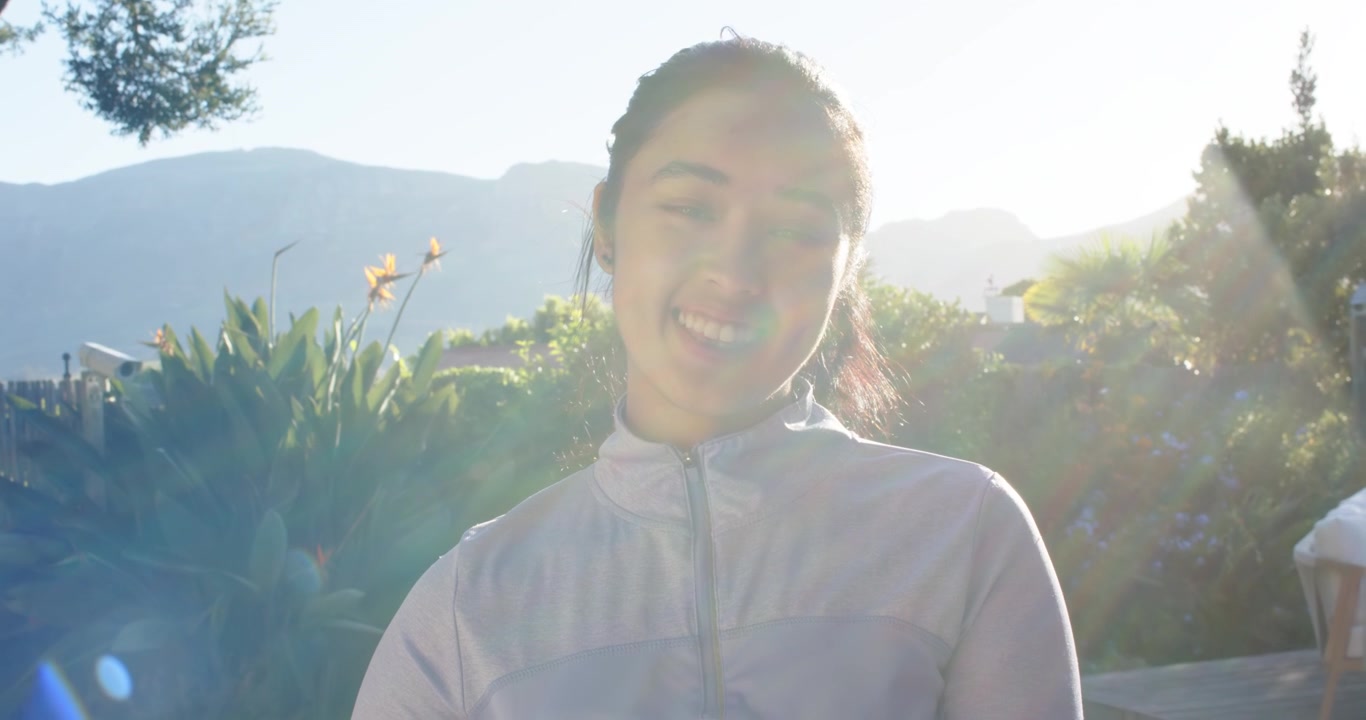 African American adult woman wearing zip top in garden reacting to lens flare turning head laughing