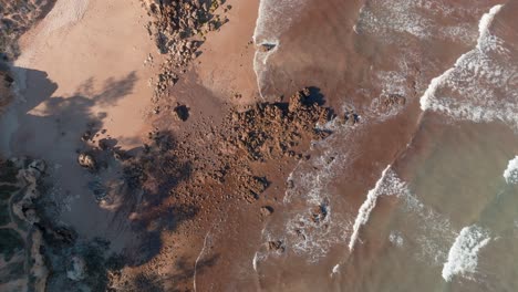 top view of ocean waves crashing on sandy golden brown shores in praia de santa eulalia