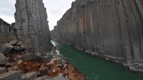 Weite-Aufnahme-Der-Basaltschlucht-Mit-Grünem-Fluss-Und-Orangefarbenem-Strom,-Der-In-Den-Hauptstrom-Fließt