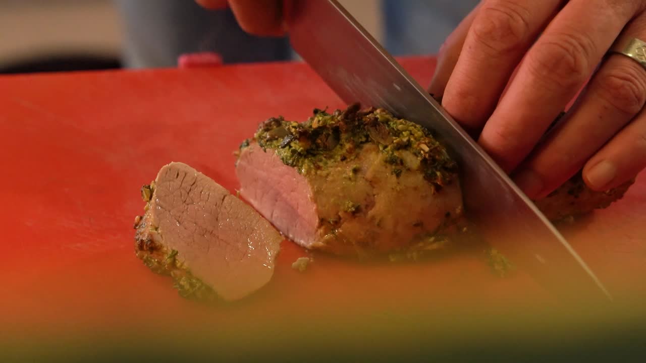 Person slicing small loaf of meat with large chef's knife. Close up.